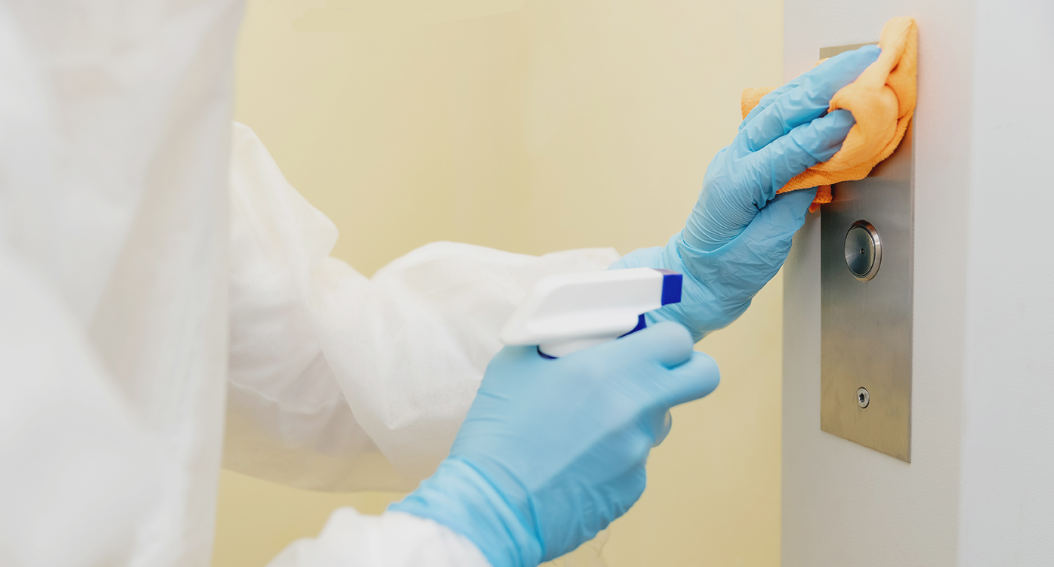 BCS technician in protective gloves sanitising a high touch lift button panel